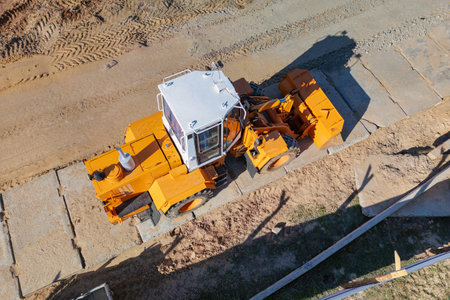 A construction truck of yellow and white colors parked on top of a dirt field under the clear sky....