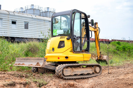 A bright yellow excavator stands still on a vast dirt field, ready for excavation or construction work.の写真素材