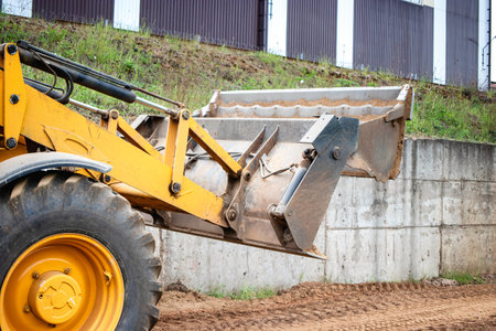 A yellow construction vehicle or a loader is parked next to a cement wall at a construction site.の写真素材