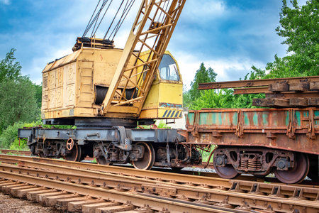 A yellow crane is perched atop train tracks, ready for construction work or maintenance.の写真素材