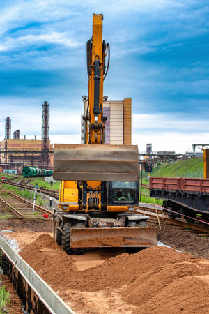 A construction site with a excavator lifting materials, surrounded by train tracks. Machinery and workers are visible on site.の写真素材