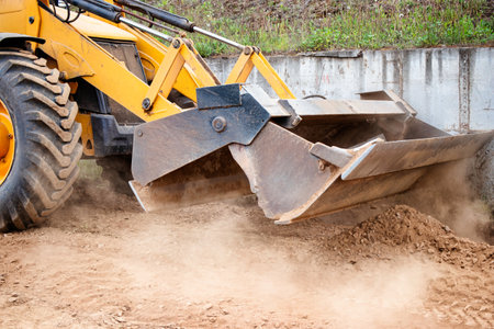 A yellow bulldozer or a loader is actively digging up dirt in a field, creating a cloud of dust with its powerful movements.の写真素材