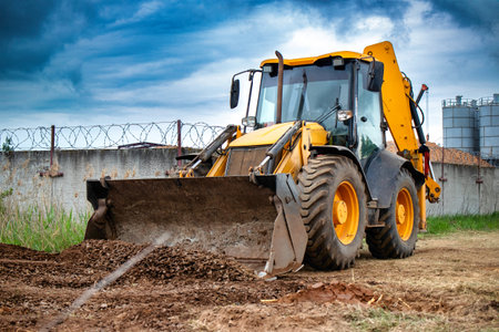A bulldozer or a loader is actively digging dirt in front of a sturdy barbed wire fence, showcasing industrial activity and security measures.の写真素材