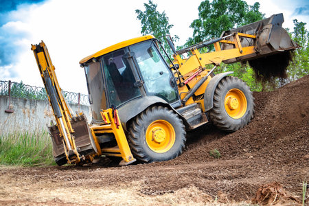 A big yellow loader is seen driving down a dusty dirt road, kicking up clouds of dust as it moves along.の写真素材