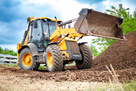 A yellow bulldozer or a loader is actively digging dirt in a field, moving and displacing soil to clear the area for construction or agricultural purposes.の写真素材