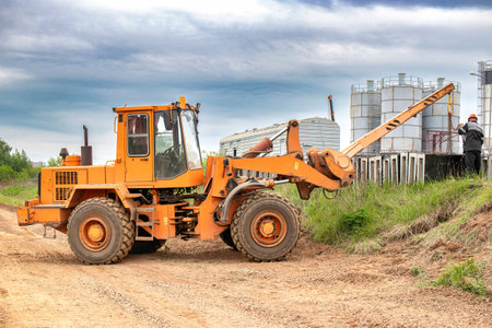 A tractor or forklift is stationary on the side of a dusty rural road, surrounded by fields and under a clear sky.の写真素材