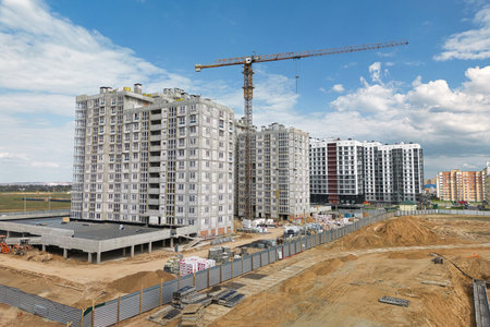 A bustling construction site with workers in hard hats, machinery moving materials, and a towering crane in the background overseeing the building process.の写真素材