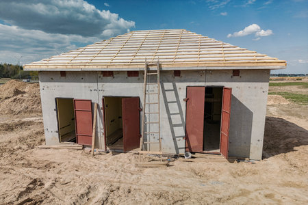 A small house under construction, surrounded by tools and materials, with a ladder leading to the roof as work progresses.の写真素材