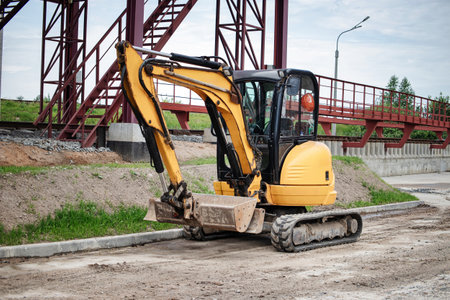 A mini excavator is actively working at an industrial plant, moving soil and materials in a busy construction area under clear skies.の写真素材