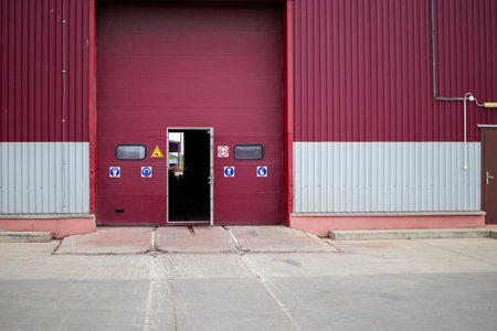 The entrance features a large red and gray gate with an open door, leading into a small industrial workshop filled with activity.の写真素材