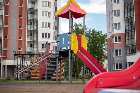 A vibrant playground features a slide and climbing structure set amidst residential buildings,...