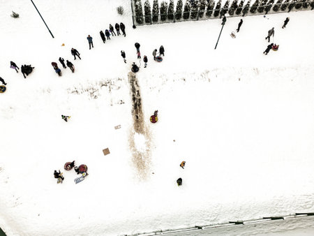 Groups of people engage in winter activities like sledding and playing in the snow, creating a lively atmosphere in the park.の写真素材