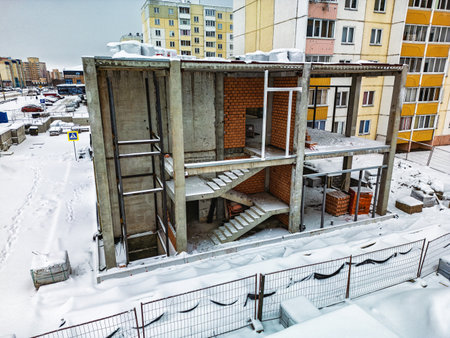 A partially constructed building stands in a snowy landscape, surrounded by construction materials and residential structures.の写真素材