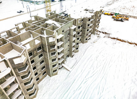 New residential construction in a snowy landscape, highlighting unfinished concrete buildings and construction equipment nearby.の写真素材