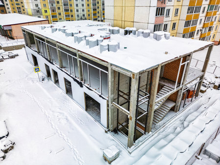 A partly completed building remains blanketed in snow, surrounded by colorful residential apartments under winter conditions.の写真素材