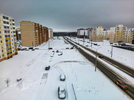 Snow blankets the ground in a suburban neighborhood with parked cars lining the road and residential buildings in the background.の写真素材