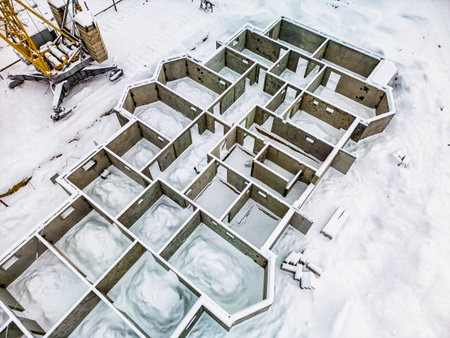 Newly constructed concrete foundation is covered in snow at a winter construction site, showing the framework of future buildings.の写真素材