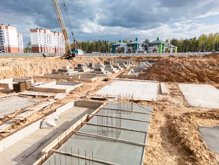Activity unfolds as workers lay the foundation for a new building, surrounded by an unfinished landscape and looming clouds above.の写真素材