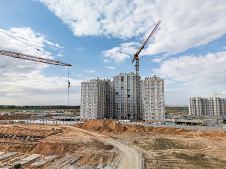 Cranes tower over new residential buildings as construction progresses under a bright sky, signaling growth in urban development.の写真素材