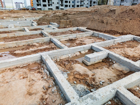 A construction site features new concrete foundations amid earth and materials under a clear sky.の写真素材