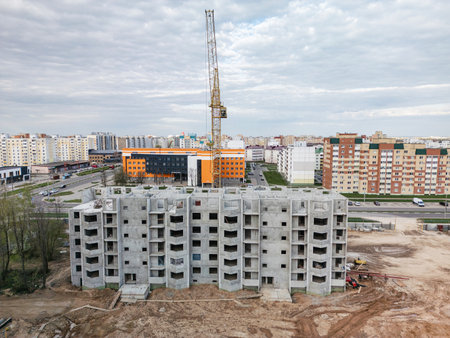 A new residential building with exposed concrete and construction equipment emerges in the urban landscape.の写真素材