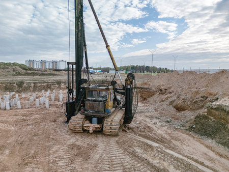 A drilling rig works at a site, digging into the ground with buildings rising in the background under gray skies.の写真素材