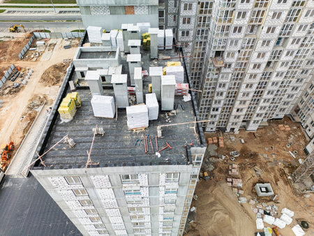 Workers are busy arranging construction materials on top of a high-rise building under a bright blue sky in a lively city.の写真素材