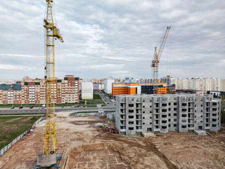 Two towering cranes stand amid an expanding city, as new residential units take shape against a backdrop of cloudy skies.の写真素材