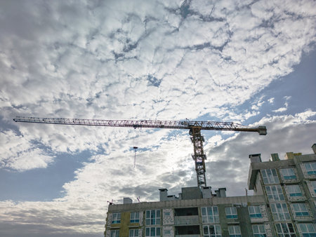A towering crane rises amid changing clouds as workers diligently continue their tasks on the new structure.の写真素材