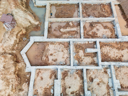 The building's foundation is forming, showing complex layouts amid muddy spots and pooled rainwater.の写真素材