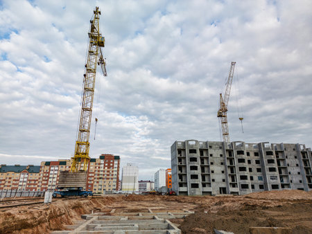 Two towering cranes work diligently, lifting materials as new buildings rise amidst a vibrant urban landscape on a cloudy day.の写真素材