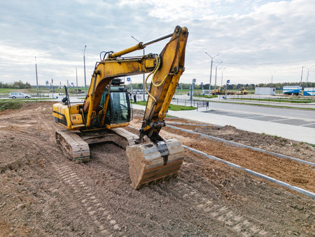 An excavator digs into the ground, preparing land for upcoming construction in a busy urban environment, with clouds overhead.の写真素材