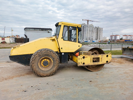 A yellow road roller sits at a construction site, amid rising urban structures and a lively atmosphere.の写真素材