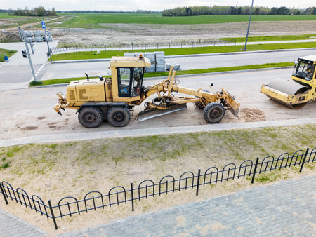 A yellow grader aligns the road while another machine prepares the surface, showcasing progress in rural street construction.の写真素材