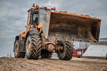 A robust loader moves earth at a busy construction site, its large bucket ready to shift soil while gray clouds loom overhead.の写真素材