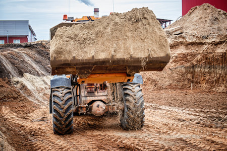 A large dump truck loaded with sand skillfully maneuvers through a construction site, leaving a...