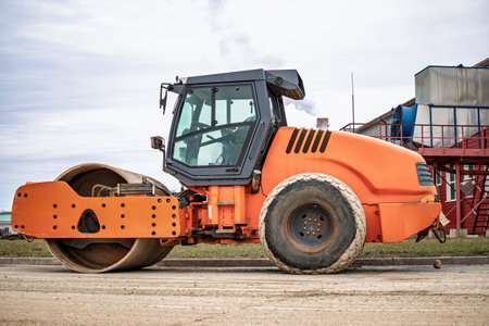 The orange road roller glides over the sand, ready to compact the ground for upcoming construction projects.の写真素材