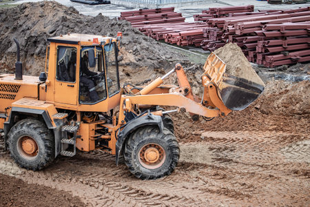 A yellow loader shifts soil at a construction site, surrounded by material and earth, showcasing the day's progress.の写真素材