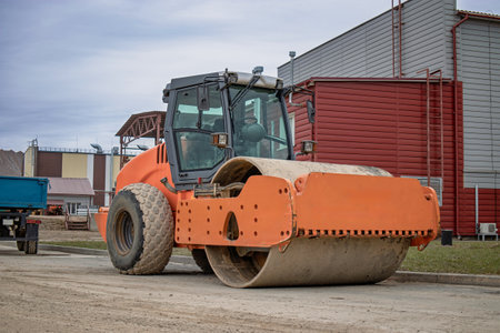 An orange roller stands idle, awaiting the next task, against a backdrop of an industrial setting and evening clouds.の写真素材