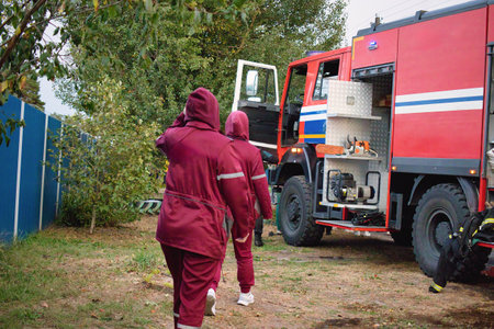 Wearing matching protective suits, emergency responders walk toward a fire truck, preparing for...