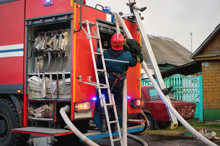 In a rural setting, a firefighter methodically organizes hoses and gear on a fire truck, the sun...