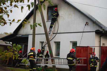 Firefighters equipped with helmets and gear work diligently outside a residential building,...
