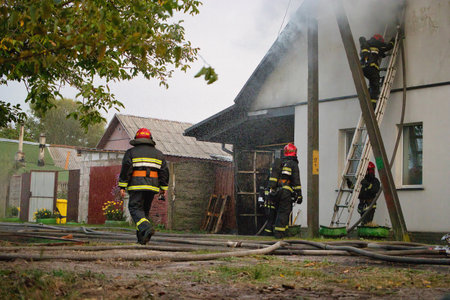 Firefighters work diligently to extinguish a fire in a rural area, skillfully navigating ladders and hoses while ensuring safety for all involved.の写真素材