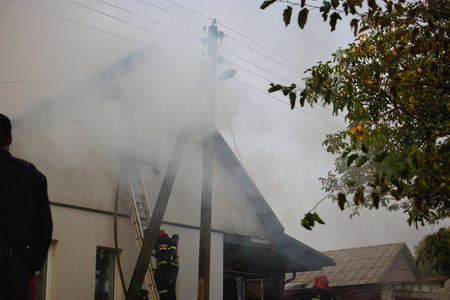 Firefighters take swift action in a busy urban neighborhood as smoke rises from a building, creating a tense and dramatic atmosphere in broad daylight.の写真素材