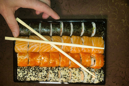 A hand reaches for a vibrant sushi platter filled with colorful rolls, featuring fresh fish and unexpected ingredients, inviting a memorable dining experience.の写真素材
