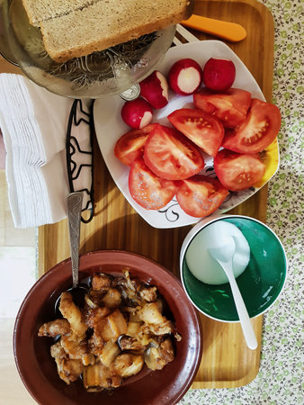 A delightful breakfast spread features roasted potatoes and onions, alongside fresh tomatoes and radishes, all served on a charming wooden tray.の写真素材