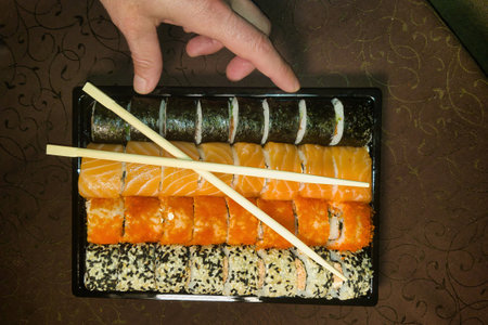 A vibrant sushi platter displays an assortment of fresh rolls and sashimi, beautifully arranged on a dark plate, as a hand extends toward a piece ready to savor.の写真素材