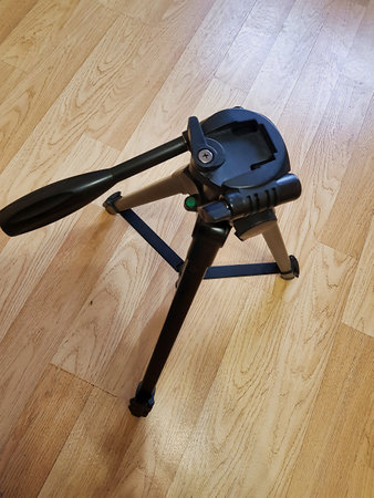 A sturdy tripod stand rests on a polished wooden surface, its legs extended evenly. The light streaming through nearby windows highlights the sleek design and sturdy build.の写真素材