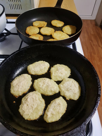 Two frying pans are filled with fritters cooking to a perfect golden brown, filling the kitchen with delightful aromas during a cozy evening.の写真素材