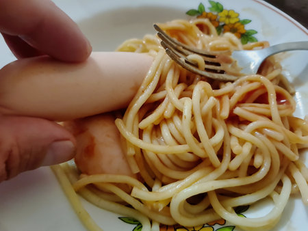 In a warm kitchen, someone holds a quirky food item while enjoying a plate of spaghetti, creating a lighthearted and amusing dining experience with unexpected elements.の写真素材